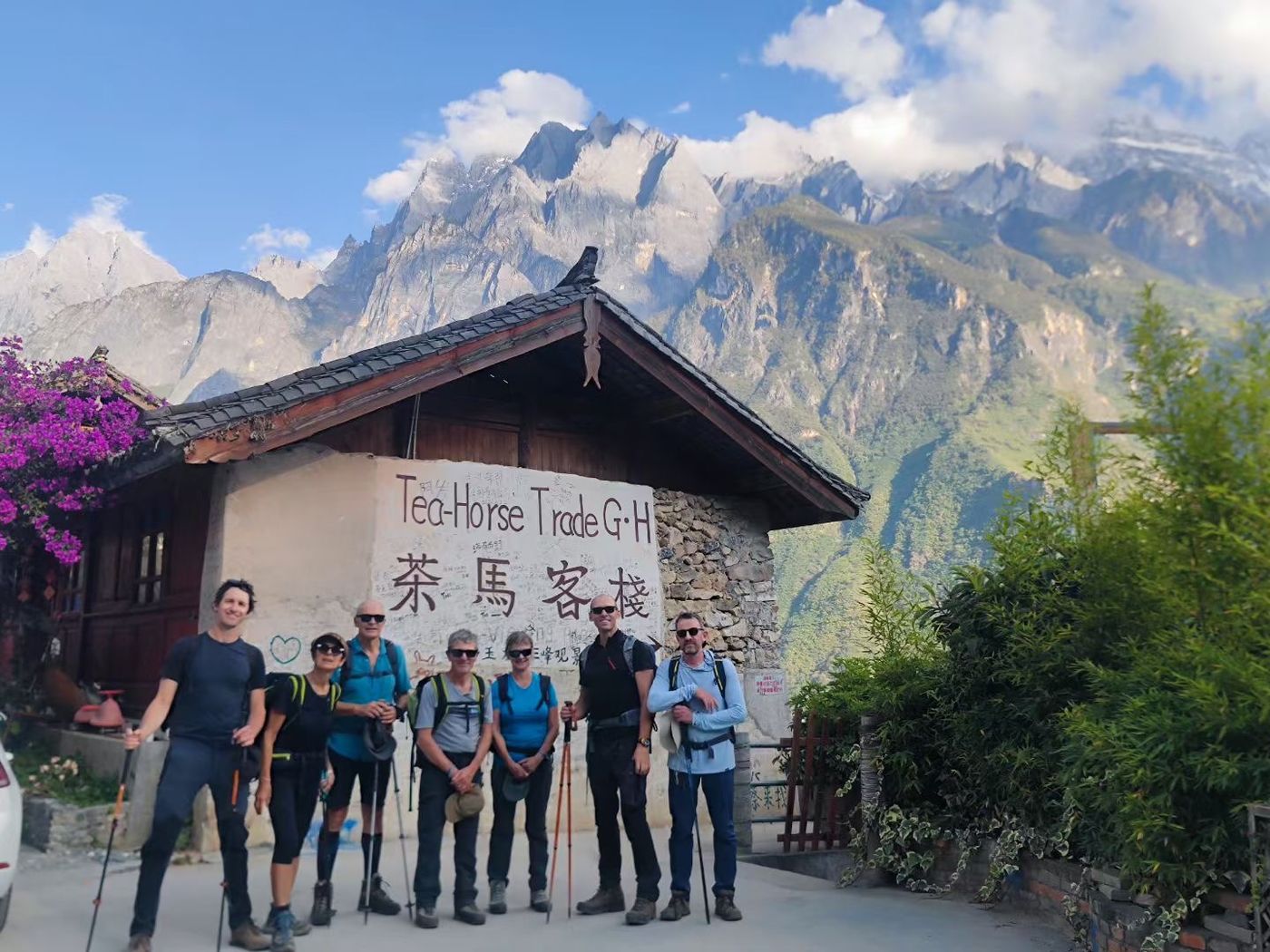 A group of seven hikers in front of the Tea Horse Trade Guesthouse, with the Jade Dragon range behind